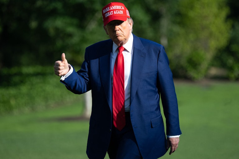 Donald Trump wears a MAGA hat and gives a thumbs up while walking outside the White House