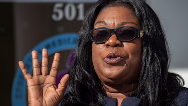 A woman holds up a hand while speaking.