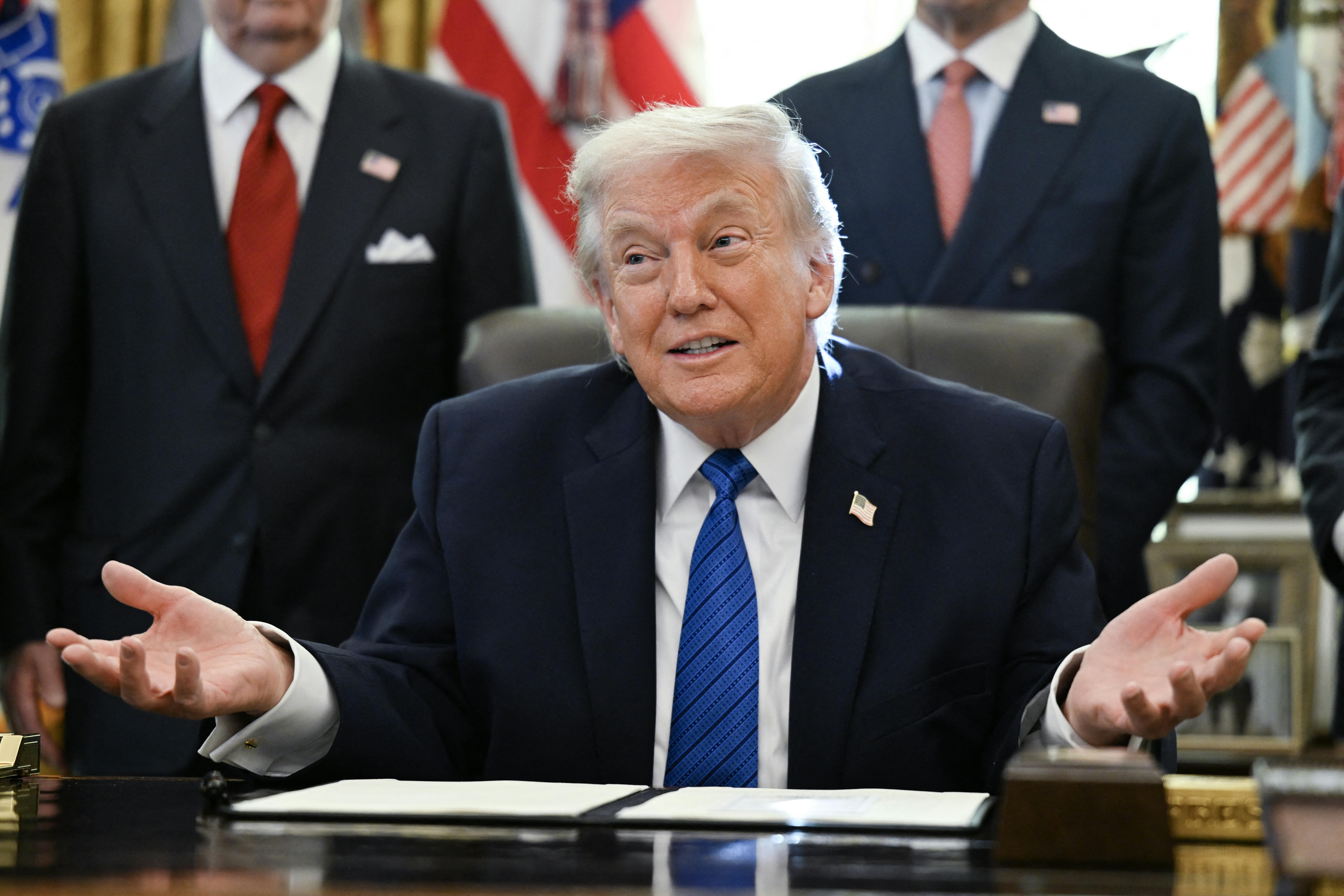 Donald Trump makes a shrugging motion while sitting at his desk in the Oval Office