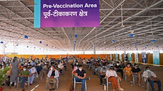 Lines of masked people sit in chairs.
