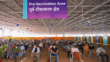 Lines of masked people sit in chairs.