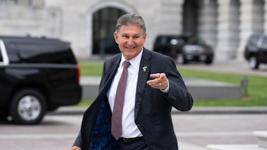 Joe Manchin grins and points as he walks.
