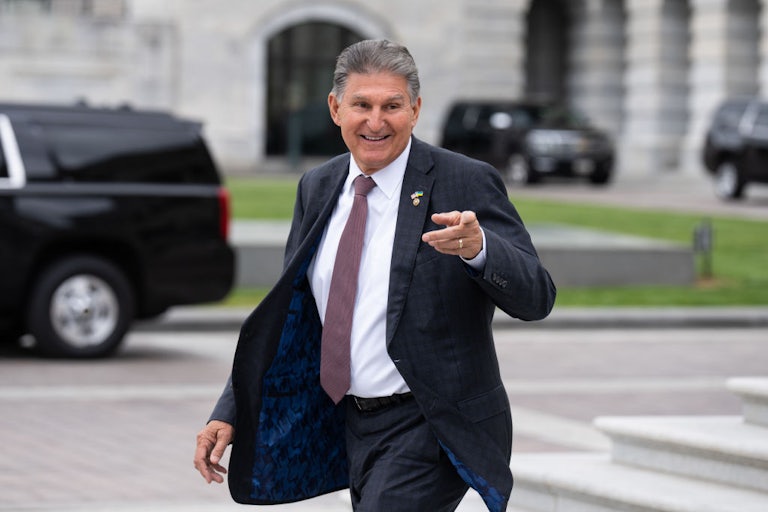 Joe Manchin grins and points as he walks.
