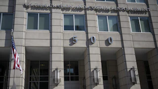 The ICE headquarters building, reading IMMIGRATION AND CUSTOMS ENFORCEMENT above the number 500 across the building's concrete front, with a flagpole on the side.