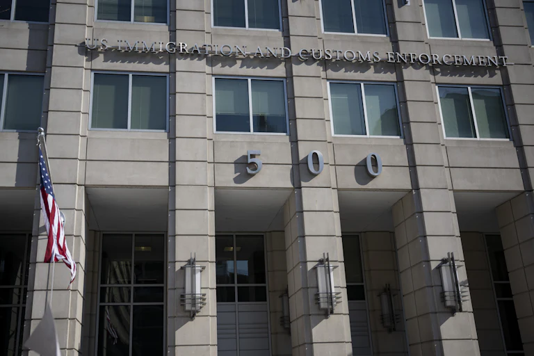 The ICE headquarters building, reading IMMIGRATION AND CUSTOMS ENFORCEMENT above the number 500 across the building's concrete front, with a flagpole on the side.