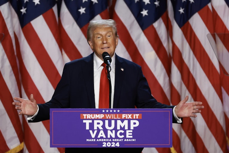 Donald Trump holds his arms out while speaking at a podium