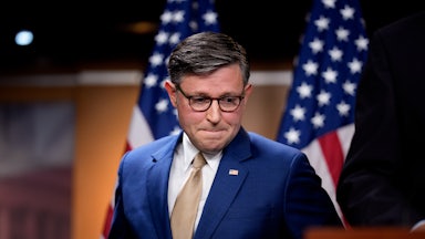 House Speaker Mike Johnson presses his lips together and looks down while standing next to a podium