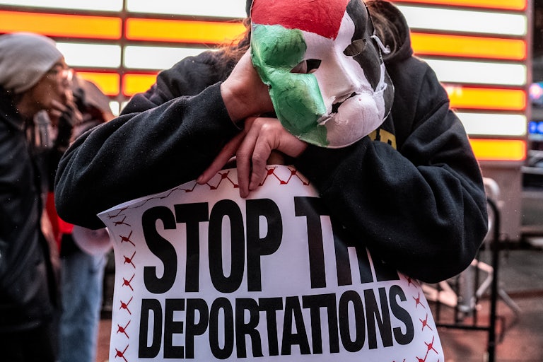 A person holds up a sign that says, "Stop the deportations" and a mask painted with the Palestinian flag during a protest in Times Square