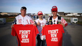 Two guys hold up red shirts that say "Front Row Joes" while a third wearing a "Trump Forever" cap gives a thumbs up