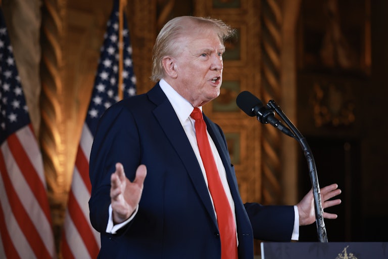 Donald Trump speaks before a mic at Mar-a-Lago and splays his hands out. Two U.S. flags are behind him.