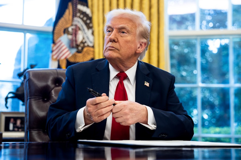 Donald Trump holds a black marker in his hand as he prepares to sign something at his desk in the White House.