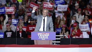RFK Jr raises his fist while standing at a podium, with fans behind him.