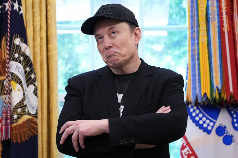 Elon Musk purses his lips and makes a dumb face while crossing his arms in the Oval Office