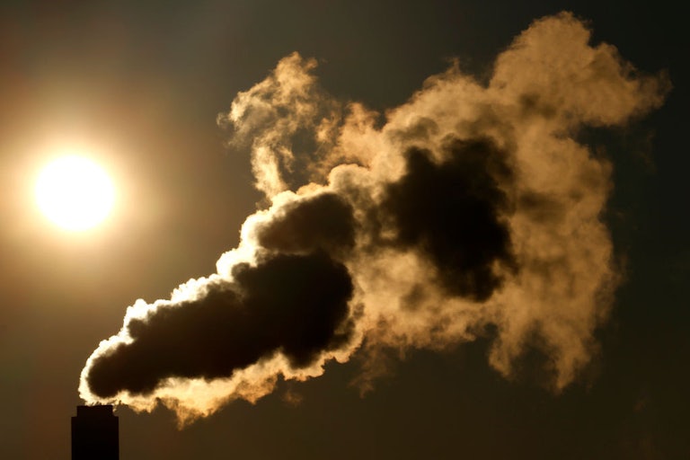 Gas pours into the sky from a smokestack, with the sun in the background.