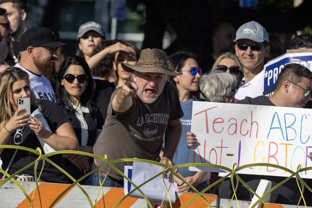 A man points at the camera while another demonstrator holds a sign reading "Tach ABC Not LGBTQ"