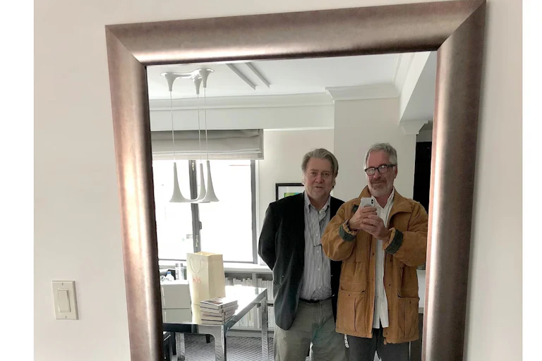 Jeffrey Epstein smiles and holds up a phone to take a photo of him and Steve Bannon as they look into a mirror.