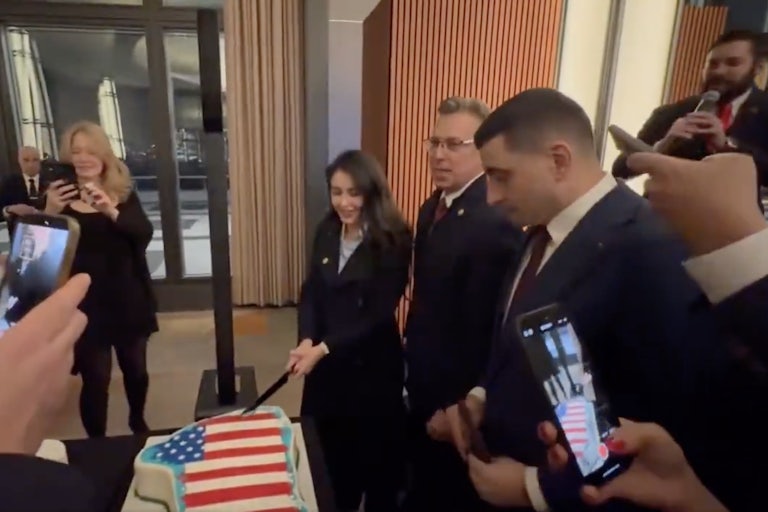 Representative Anna Paulina Luna cuts into a Greenland flag draped in the U.S. flag alongside Representative Andy Ogles and Romania's George Simion. Others hold up their cameras to record.