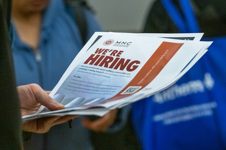 Someone holds a piece of paper that reads "We're hiring" in big, bold, red font.