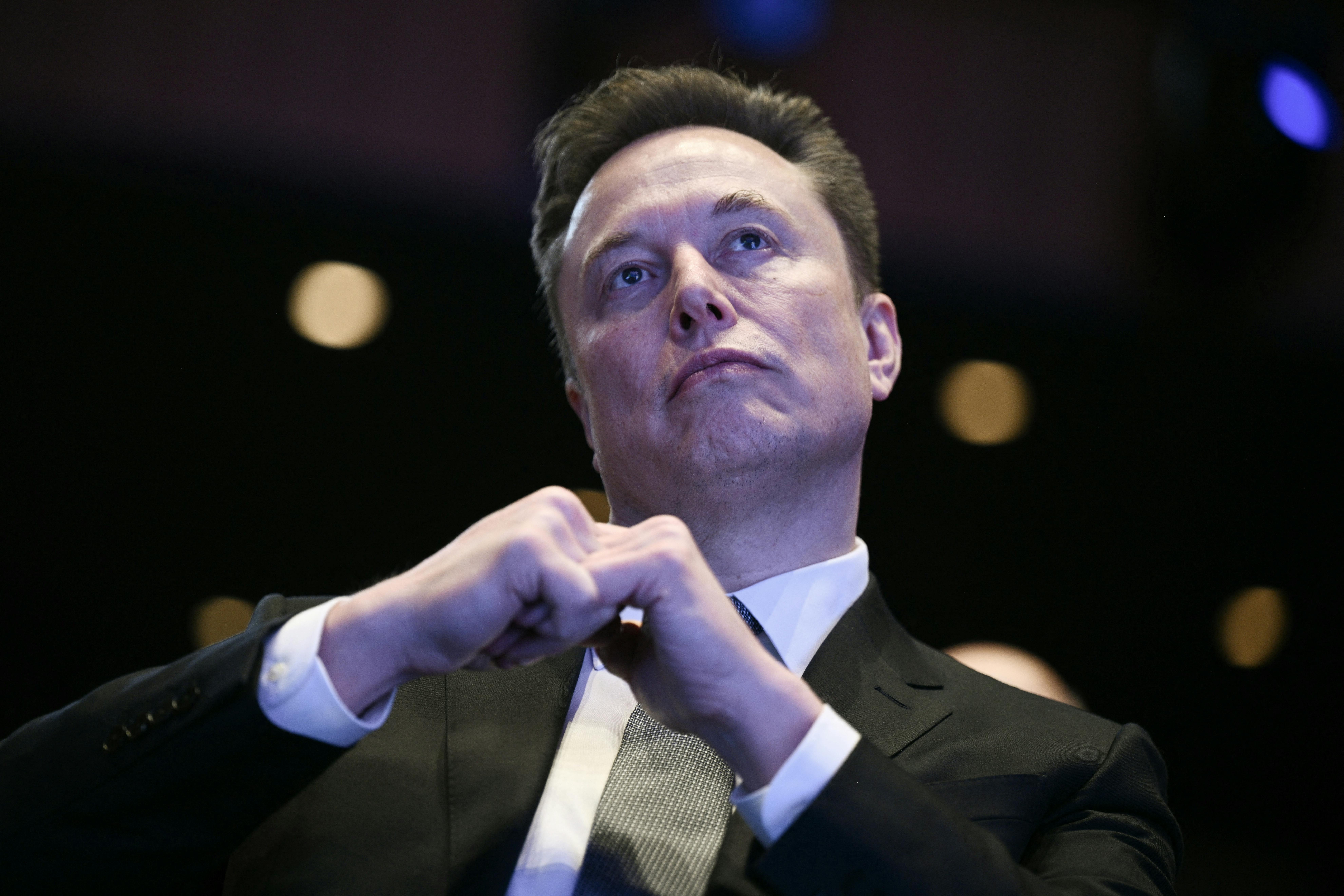 Elon Musk sits with his fingers interlaced in front of him