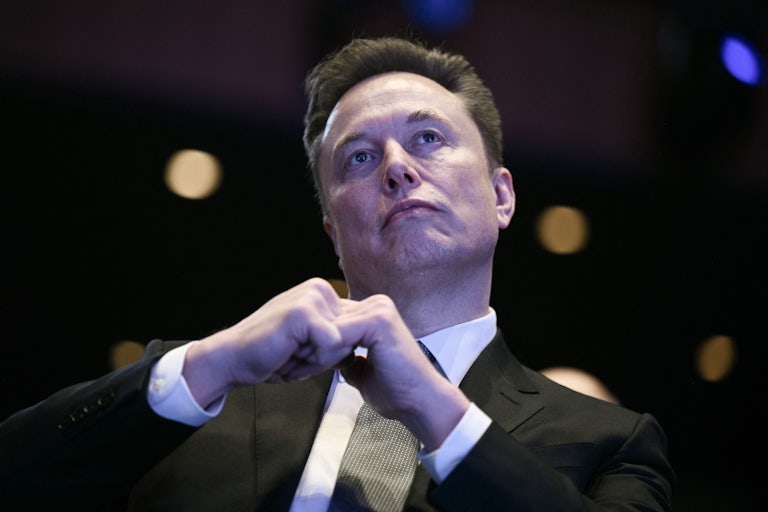 Elon Musk sits with his fingers interlaced in front of him