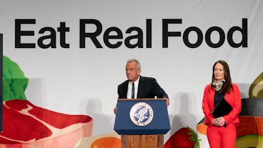 Robert F. Kennedy Jr. leans forward slightly and speaks at a podium in front of a banner that says, "Eat Real Food." Agriculture Secretary Brooke Rollins stands next to him.