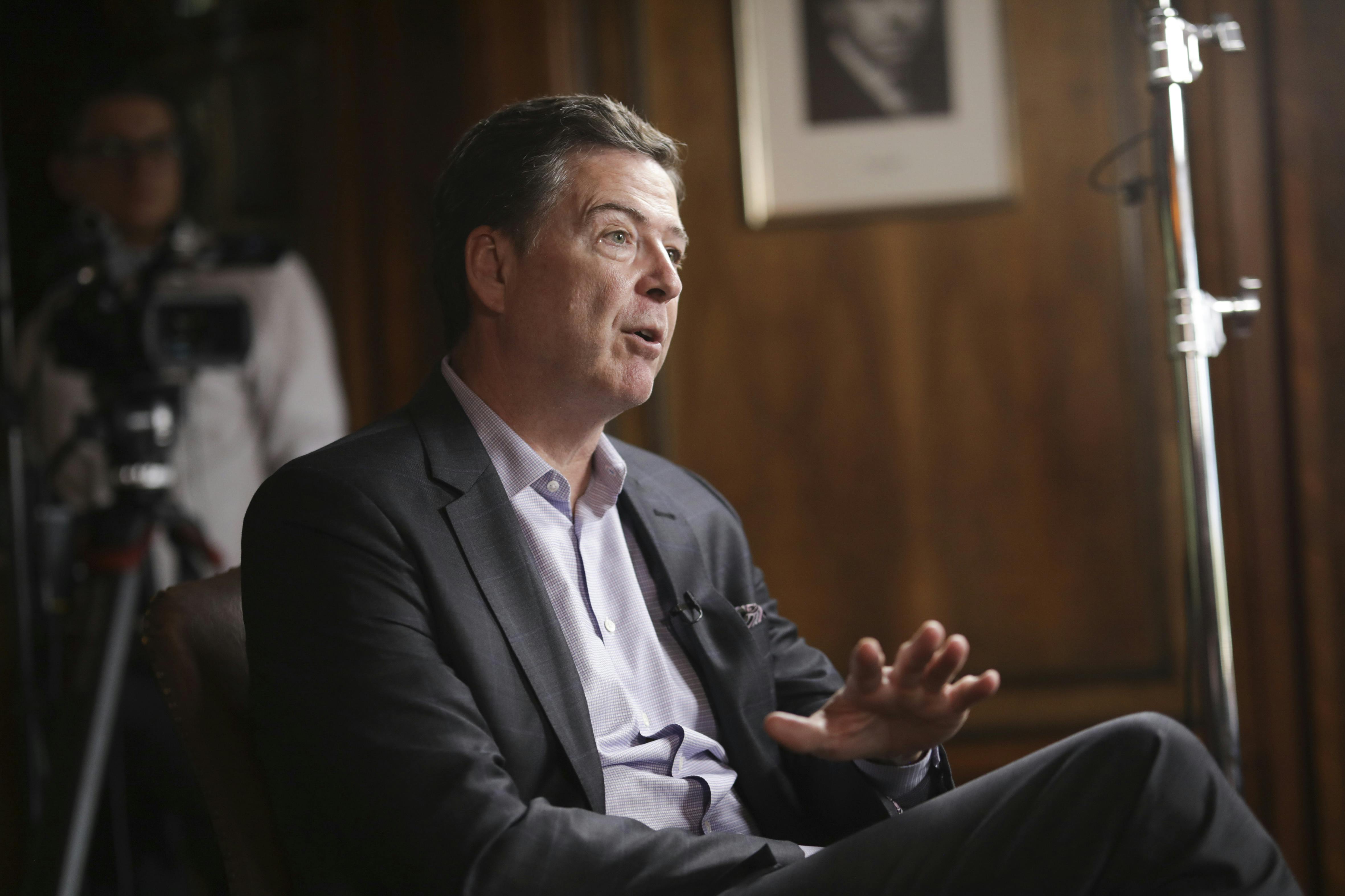 Former FBI Director James Comey gestures and speaks while sitting in a chair