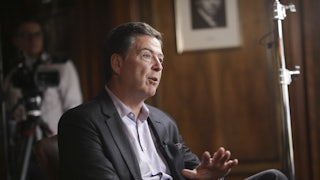 Former FBI Director James Comey gestures and speaks while sitting in a chair