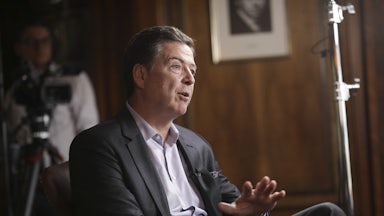 Former FBI Director James Comey gestures and speaks while sitting in a chair