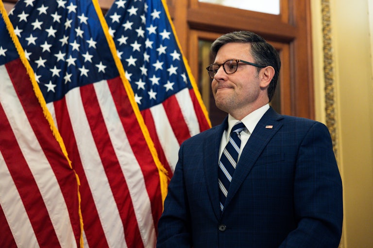 Mike Johnson grimaces while standing next to American flags