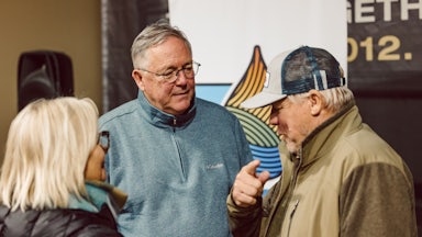 Chris Jones, wearing a blue half-zip, stands between two other people, talking to them.