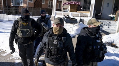 Multiple masked ICE agents walk outside in the snow.