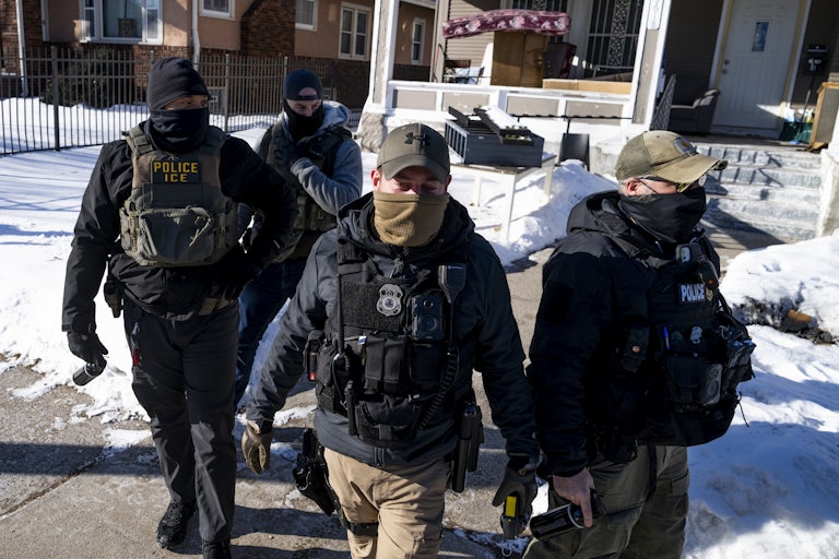 Multiple masked ICE agents walk outside in the snow.