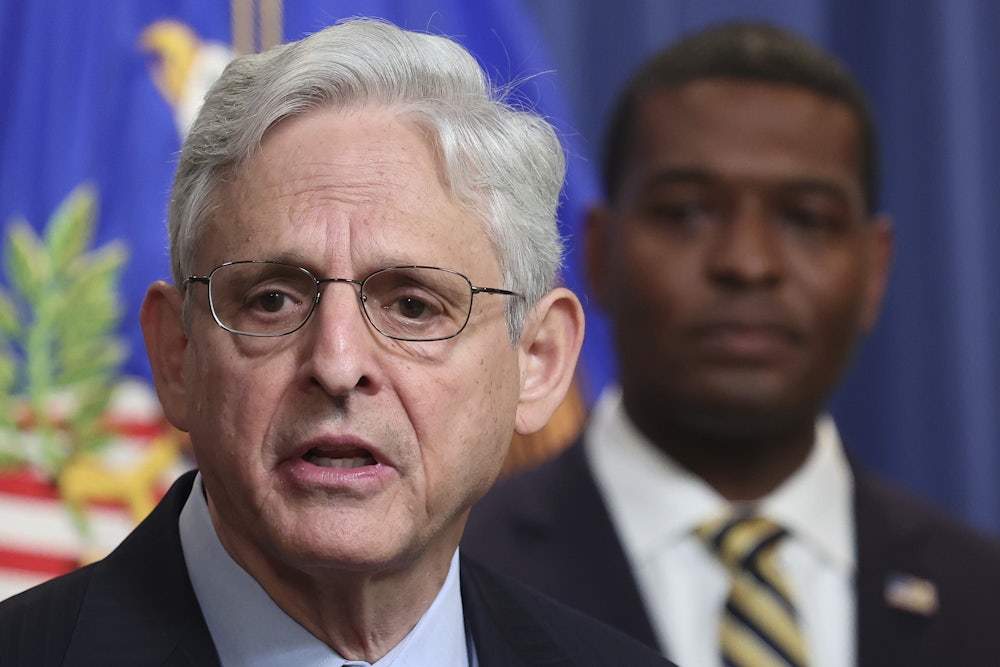 Merrick Garland speaks in foreground with Michael Regan in background.