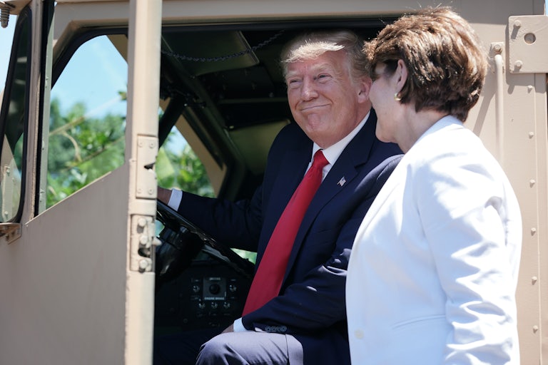 Donald Trump smiles as he sits in a THAAD anti-ballistic missile launcher. Lockheed Martin's Marillyn Hewson watches him and smiles.