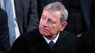 John Roberts, wearing a black robe, grimaces and looks to his right.