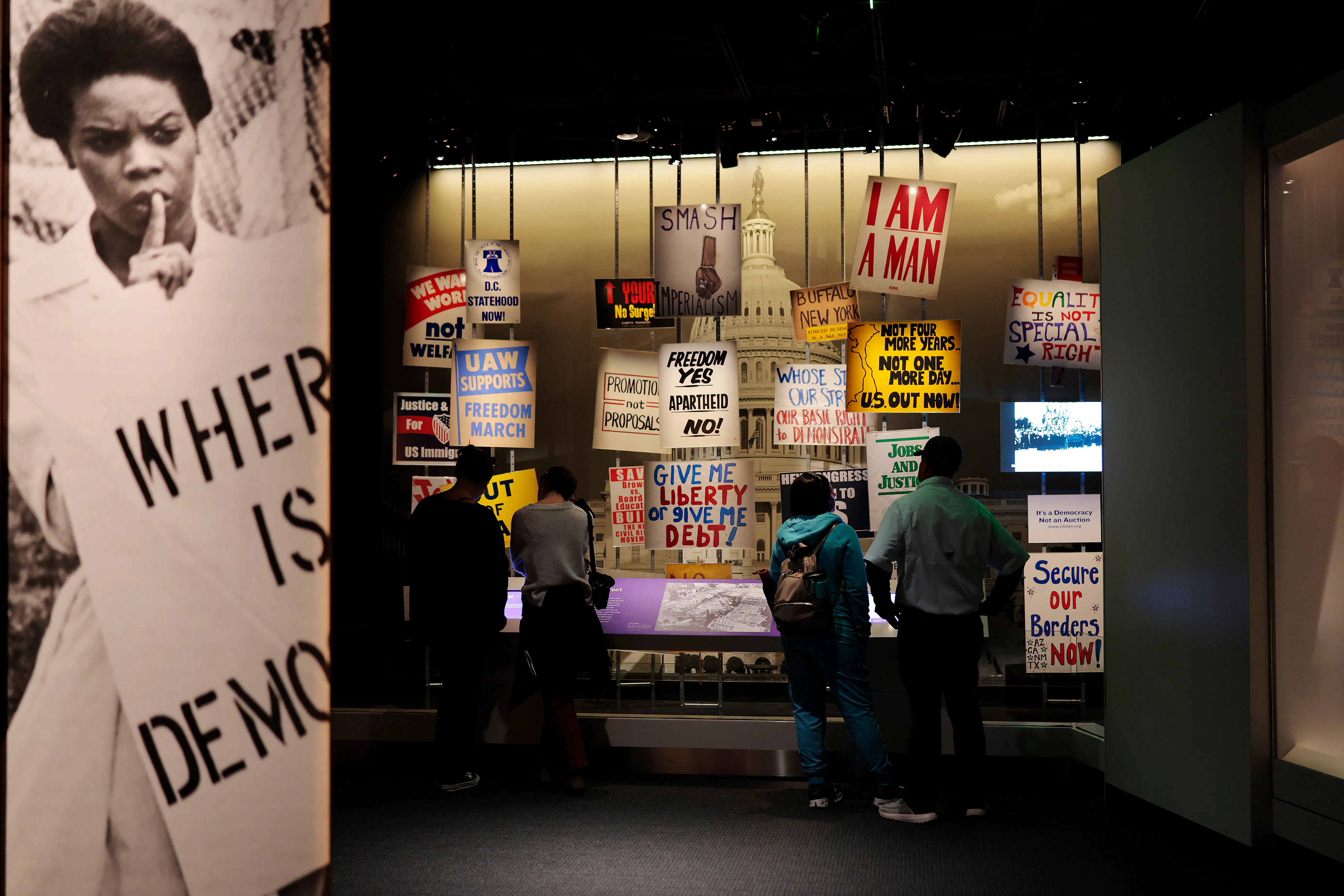 An exhibit at the National Museum of American History features signs like "Where is democracy," "Freedom Yes Apartheid No," and "Give me liberty or give me debt."