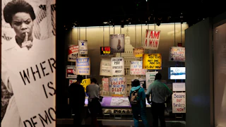 An exhibit at the National Museum of American History features signs like "Where is democracy," "Freedom Yes Apartheid No," and "Give me liberty or give me debt."
