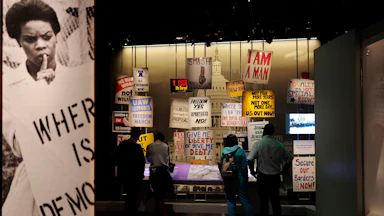 An exhibit at the National Museum of American History features signs like "Where is democracy," "Freedom Yes Apartheid No," and "Give me liberty or give me debt."