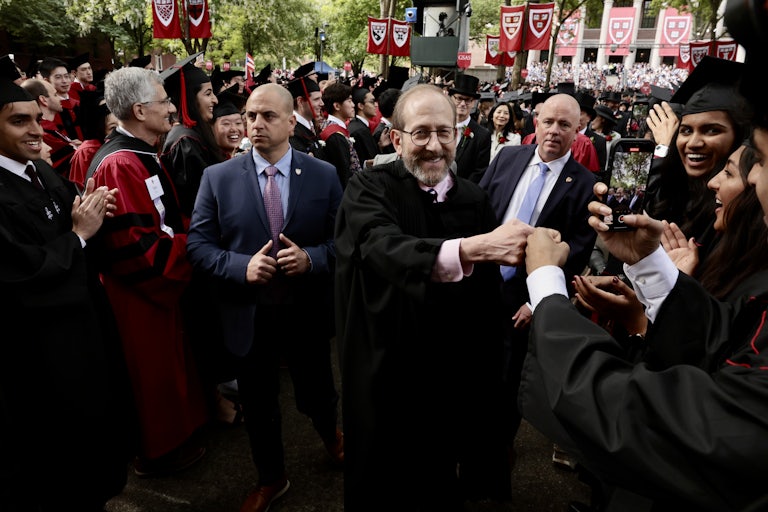 Harvard students applaud and fist-bump university President Alan Garber as he leads the graduation ceremony procession
