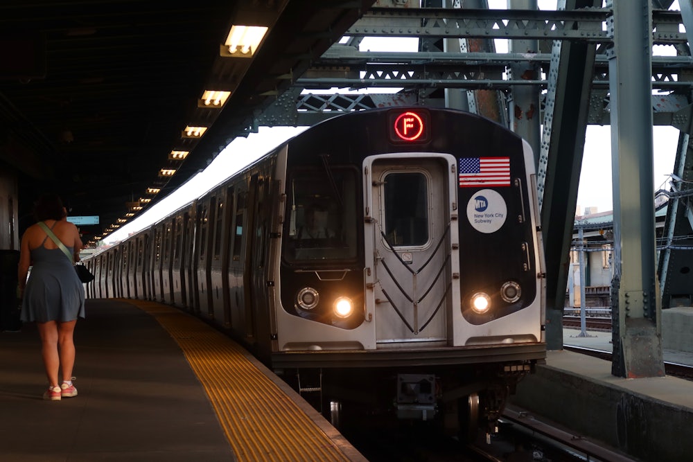A person in a dress waits as a train bearing an American flag approaches the platform.