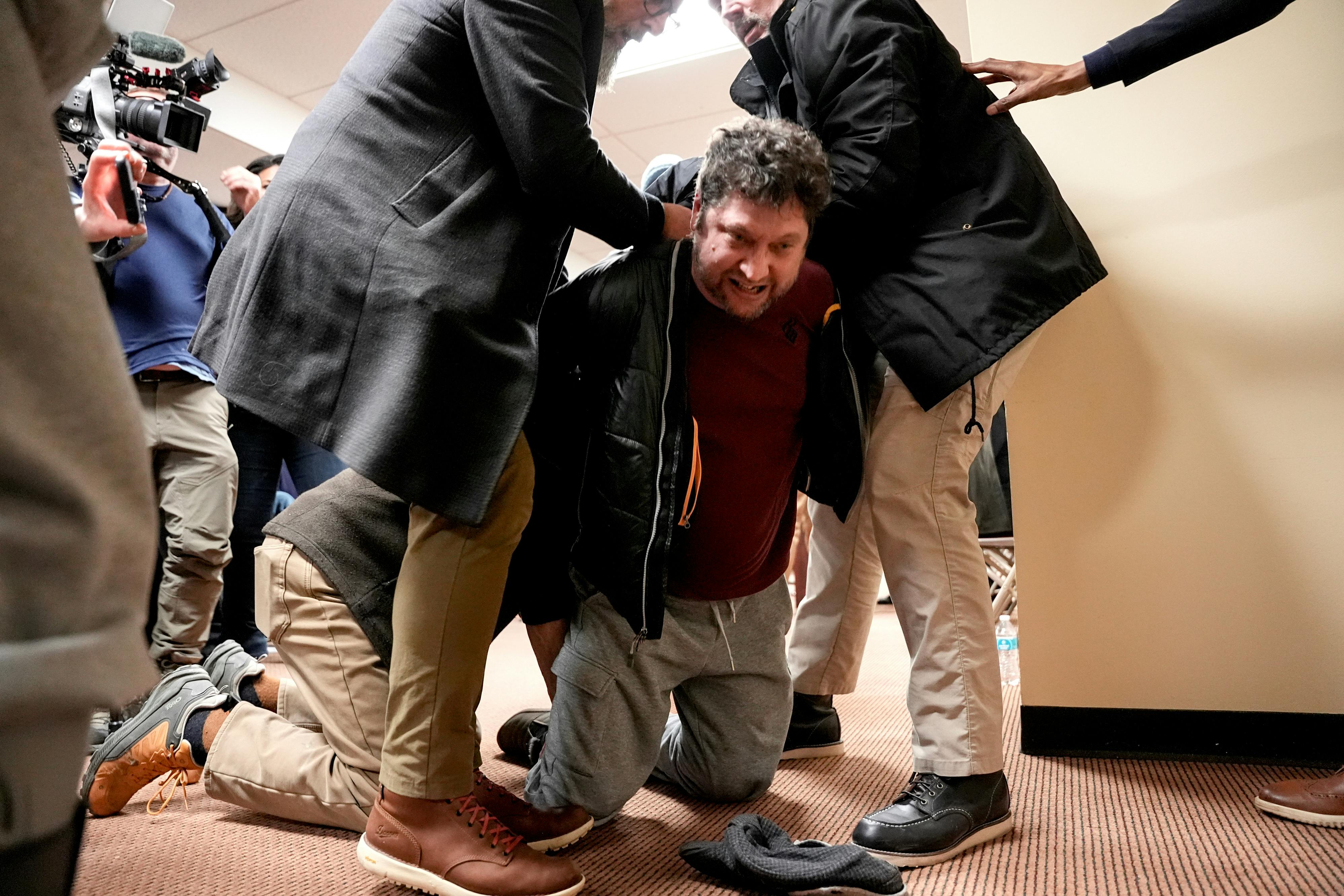 A man kneels as he is held down by three others, just after attacking Representative Ilhan Omar at a town hall.