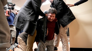 A man kneels as he is held down by three others, just after attacking Representative Ilhan Omar at a town hall.