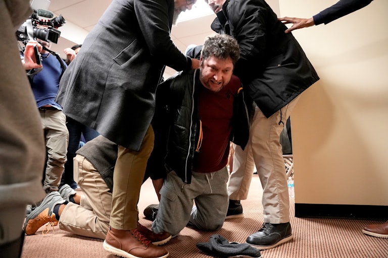A man kneels as he is held down by three others, just after attacking Representative Ilhan Omar at a town hall.
