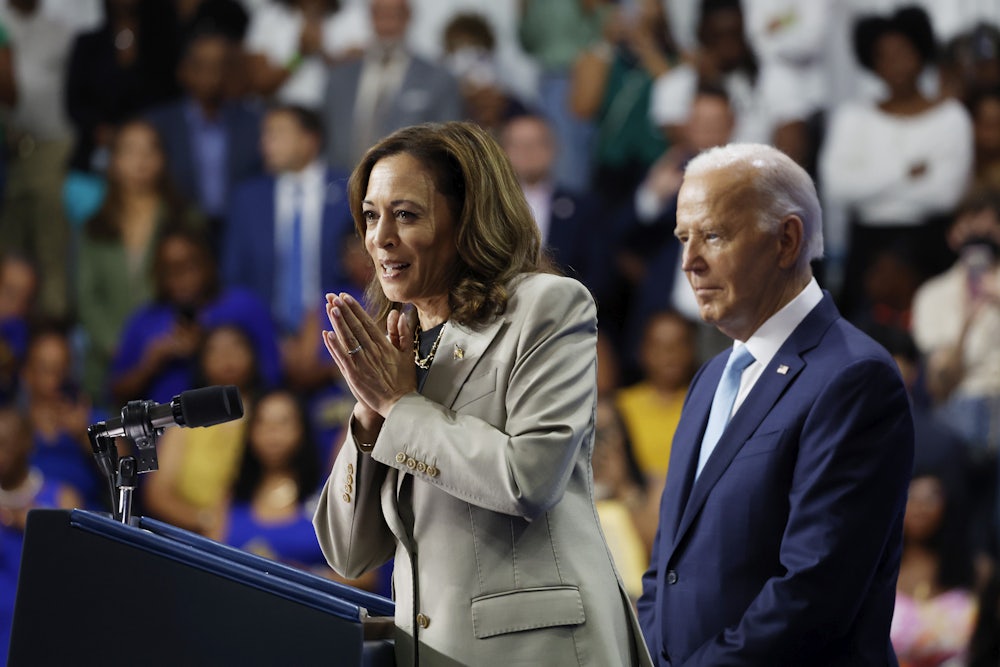 Kamala Harris presses her hands together while smiling, with Joe Biden standing to her right.