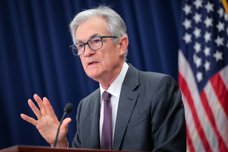 Fed Chair Jerome Powell puts up a hand while speaking at a podium.