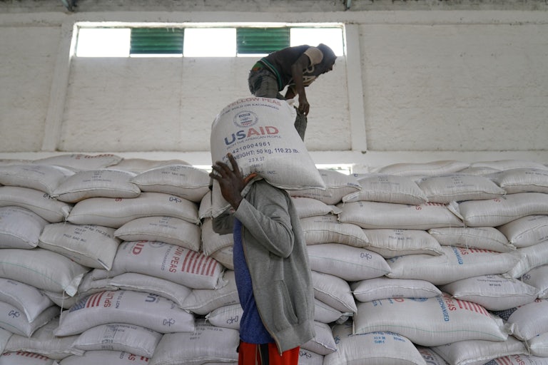 Aid workers in Ethiopia move large bags of yellow lentils labelled USAID. (There is a giant wall of them.)