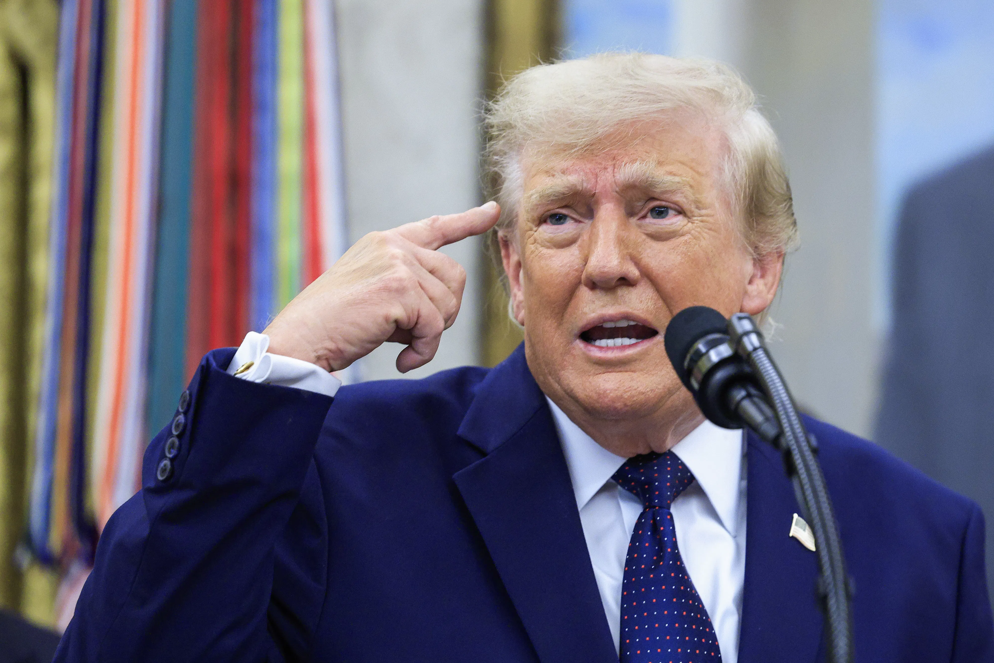 Donald Trump points his right finger at his head while grinning