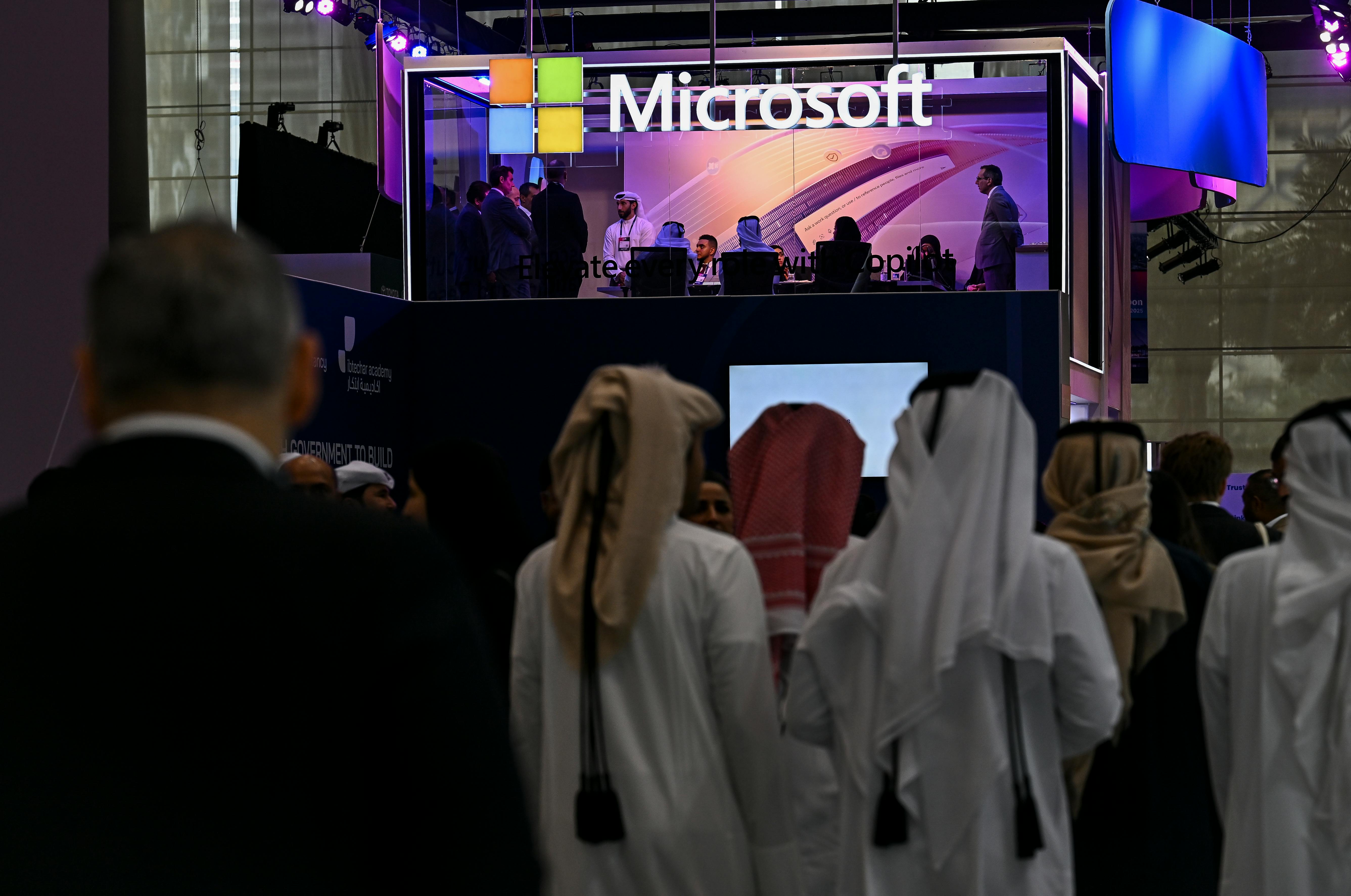 People walk past a Microsoft stand, many dressed in tradditional attire.