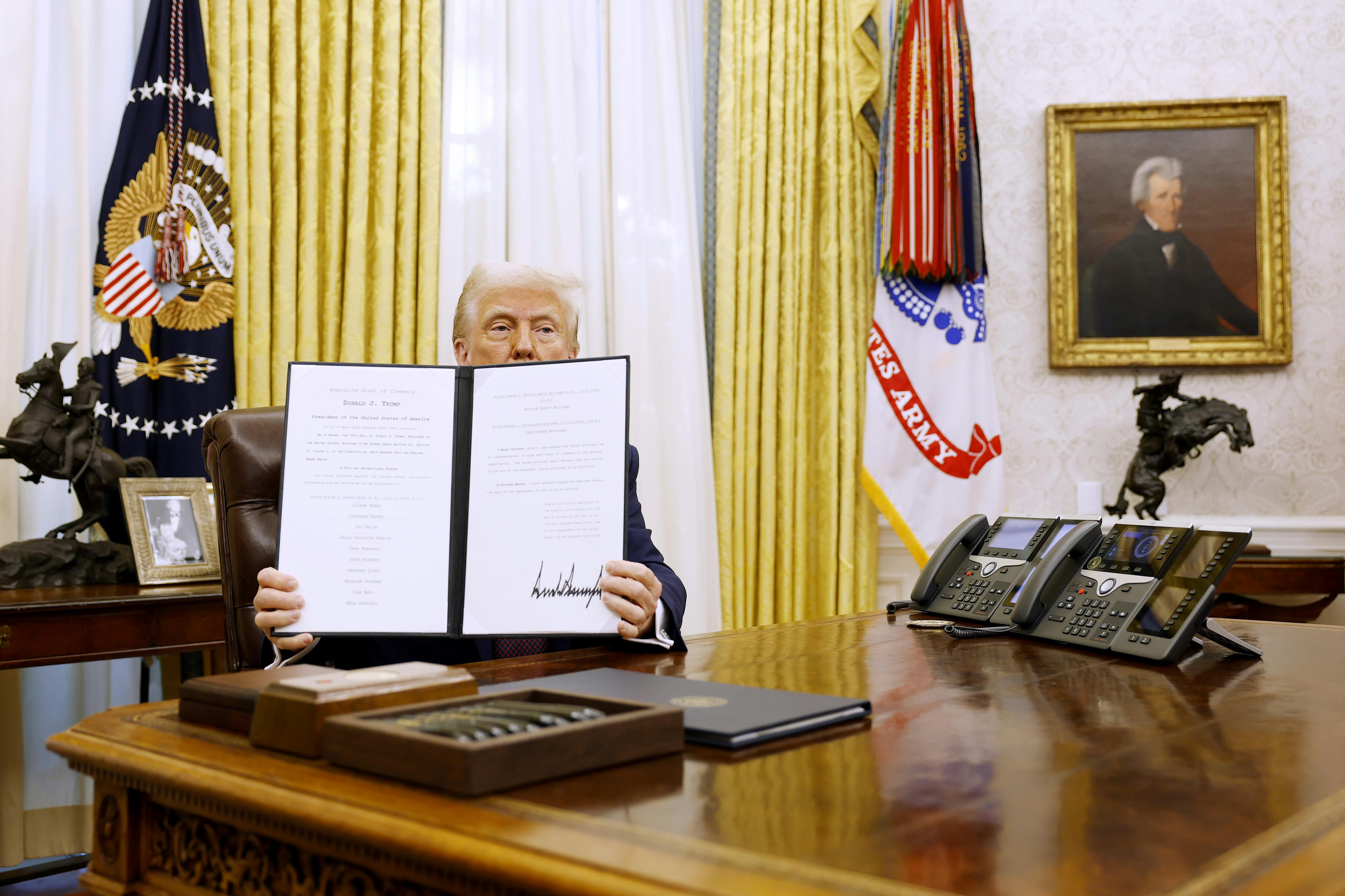  Donald Trump holds up a signed executive order in the Oval Office.