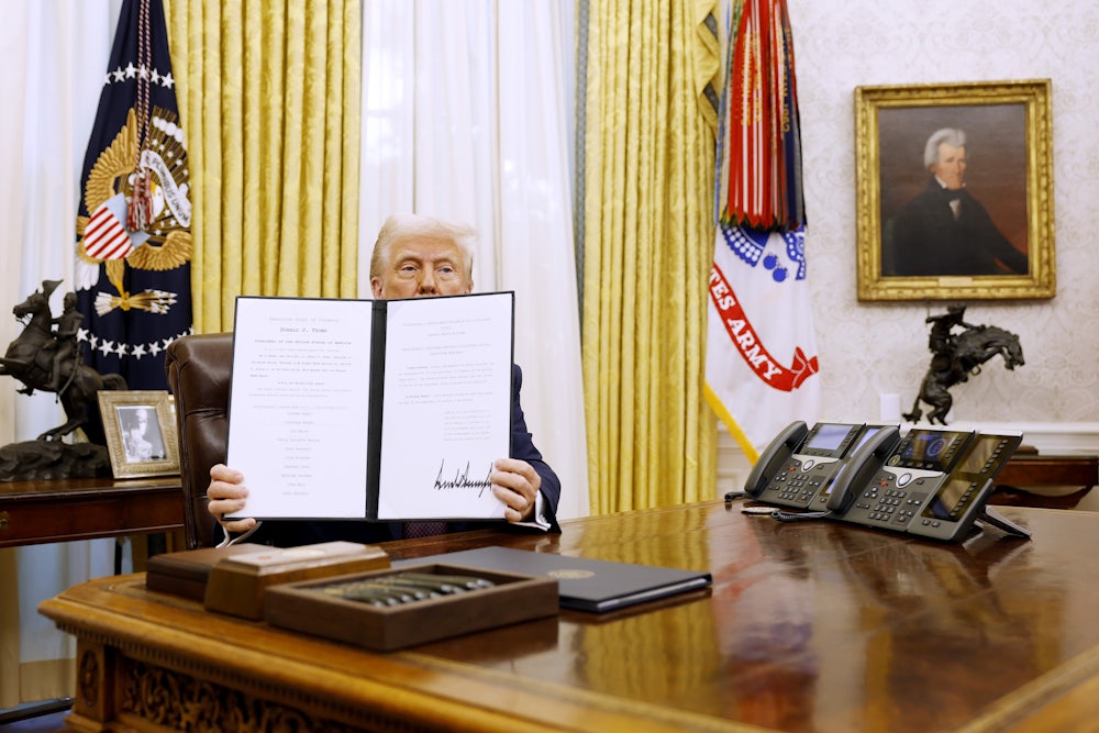 Donald Trump holds up a signed executive order in the Oval Office.